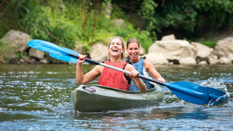 Two smiling young women kayaking down a river